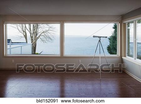 Stock Image - Telescope looking out living room window to ocean. Fotosearch