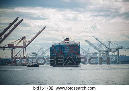 Stock Image - Tugboat and container ship in industrial harbor. Fotosearch