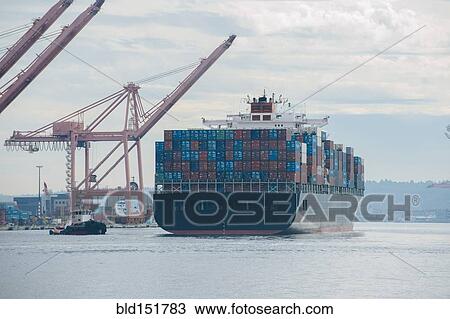 Stock Image - Tugboat and container ship in industrial harbor. Fotosearch