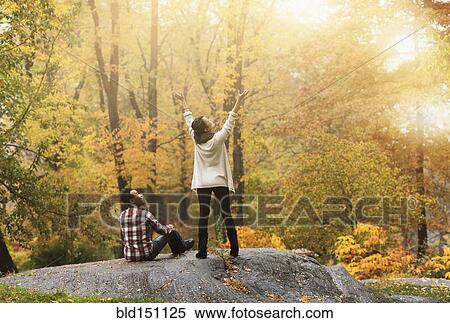 Stock Photography - Woman cheering with arms outstretched near boyfriend in park. Fotosearch