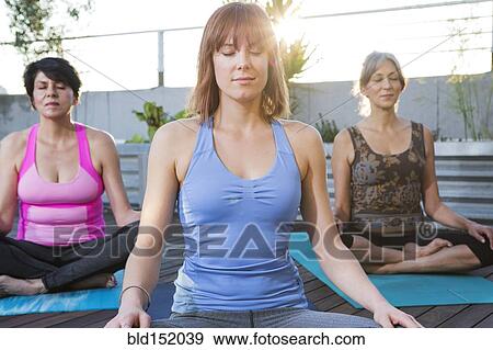 Stock Photo - Women meditating together on rooftop. Fotosearch