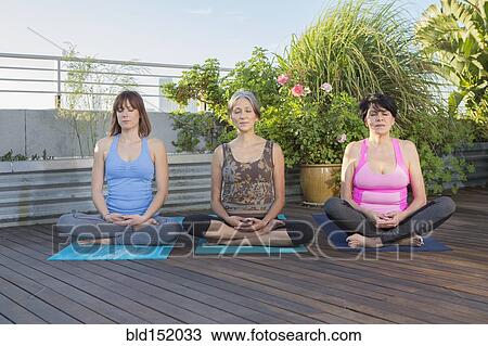 Stock Image - Women meditating together on urban rooftop. Fotosearch