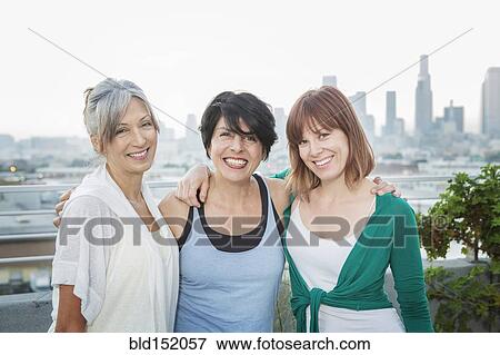 Stock Photo - Women smiling together on urban rooftop. Fotosearch