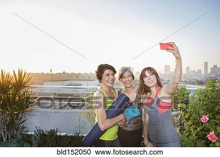 Stock Image - Women taking cell phone selfie on urban rooftop. Fotosearch
