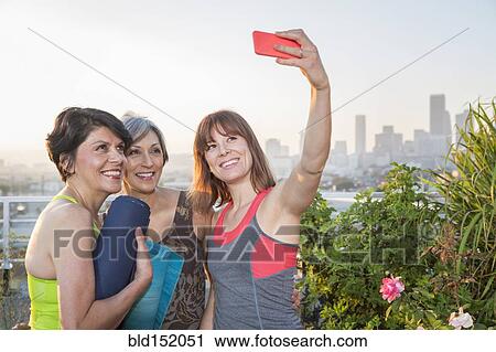 Stock Image - Women taking cell phone selfie on urban rooftop. Fotosearch