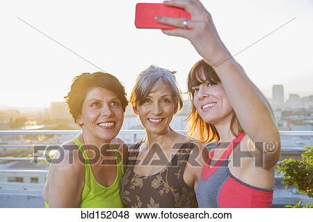 Stock Photo - Women taking cell phone selfie on urban rooftop. Fotosearch