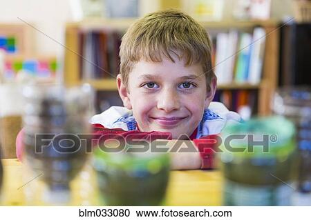 Stock Image - Caucasian boy leaning chin on desk in classroom. Fotosearch