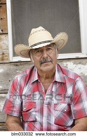 Stock Image - Hispanic man wearing cowboy hat near shed. Fotosearch