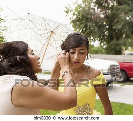 Stock Image - Hispanic mother adjusting quinceanera hairdo outdoors. Fotosearch