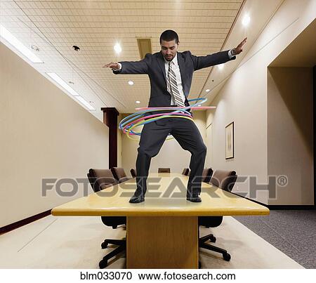 Stock Image - Mixed race businessman on conference table spinning plastic hoops. Fotosearch
