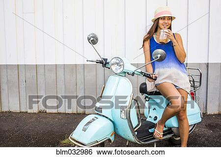 Stock Photograph - Pacific Islander woman drinking iced coffee on scooter. Fotosearch