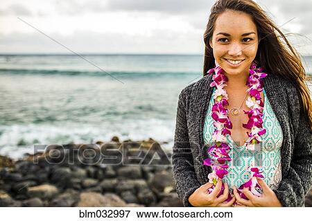 Stock Photo - Pacific Islander woman wearing flower lei near rocky beach. Fotosearch