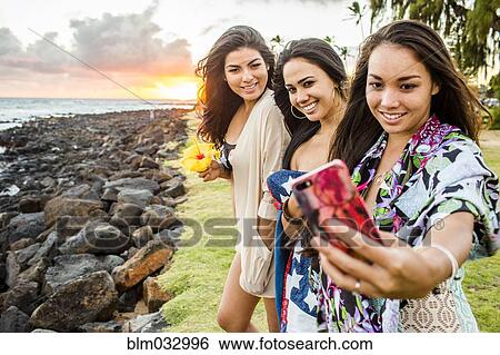 Stock Photograph - Pacific Islander women taking cell phone photograph near rocky beach. Fotosearch