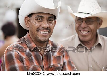 Stock Image - Smiling Hispanic men wearing cowboy hats. Fotosearch