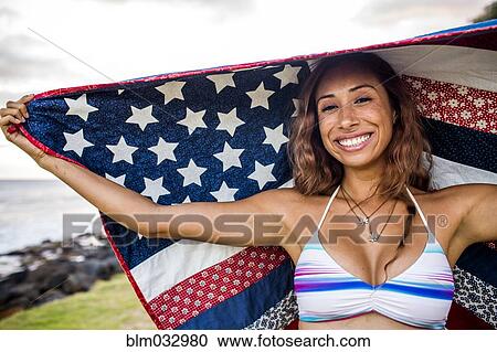 Stock Image - Woman standing under American flag quilt. Fotosearch