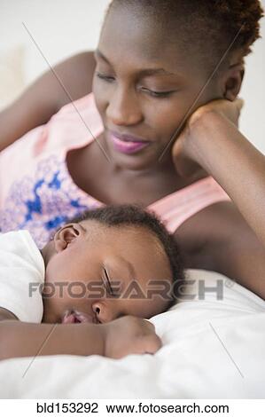Black mother admiring sleeping son on bed View Large Photo Image Stock Image - Black mother admiring sleeping son on bed. Fotosearch