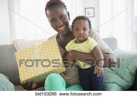 Stock Photograph - Black mother and son holding gift on sofa. Fotosearch