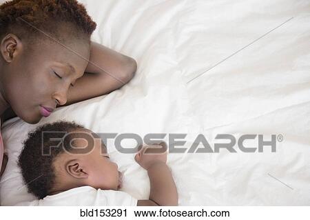 Stock Image - Black mother and son sleeping on bed. Fotosearch
