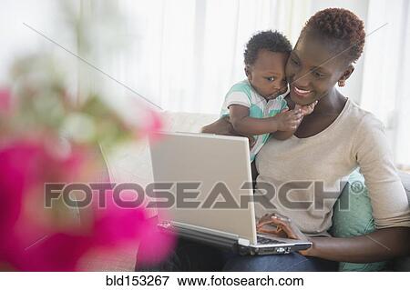 Stock Photo - Black mother and son using laptop on sofa. Fotosearch