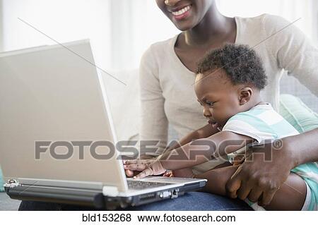 Stock Photo - Black mother and son using laptop on sofa. Fotosearch
