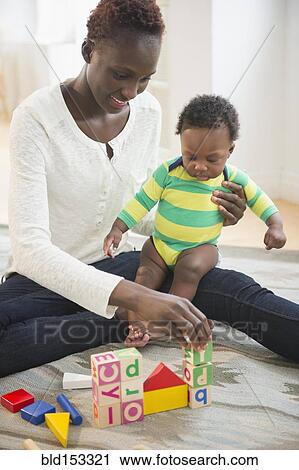 Stock Image - Black mother playing with baby boy in living room. Fotosearch