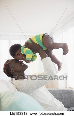 Stock Image - Black mother playing with baby boy on sofa. Fotosearch