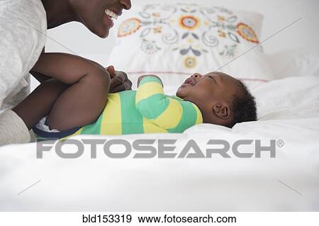 Stock Photo - Black mother playing with baby boy on bed. Fotosearch