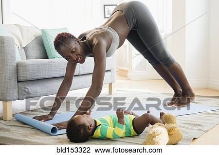 Stock Image - Black mother practicing yoga with baby boy in living room. Fotosearch