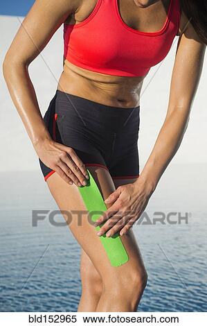Stock Photography - Caucasian athlete taping thigh near swimming pool. Fotosearch