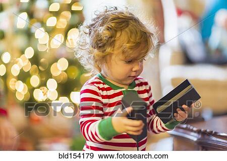Stock Photo - Caucasian baby boy opening present near Christmas tree. Fotosearch