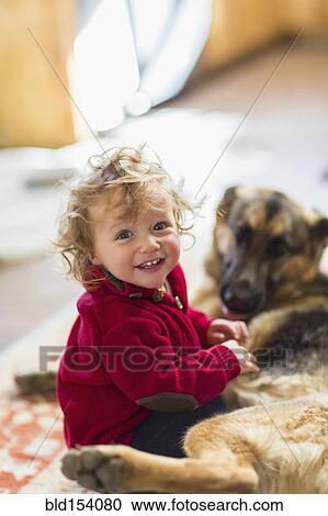 Stock Image - Caucasian baby boy playing with dog on floor. Fotosearch