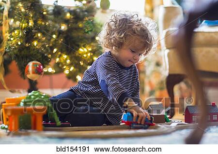 Stock Image - Caucasian baby boy playing with toys near Christmas tree. Fotosearch