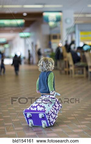 Stock Image - Caucasian baby boy rolling luggage in airport. Fotosearch