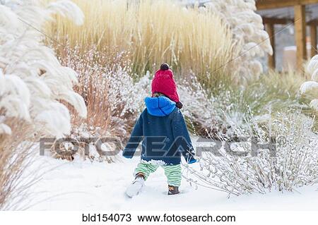 Stock Image - Caucasian baby boy walking in snowy garden. Fotosearch
