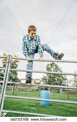 Stock Photo - Caucasian boy climbing fence on farm. Fotosearch