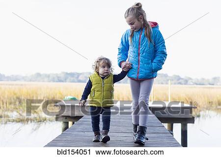 Stock Image - Caucasian brother and sister walking on wooden dock. Fotosearch