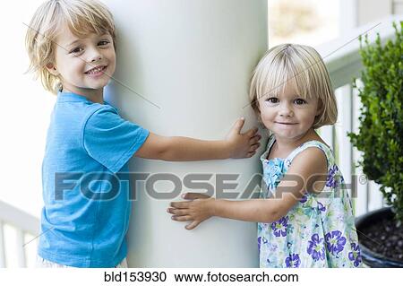 Stock Image - Caucasian children hugging column outdoors. Fotosearch
