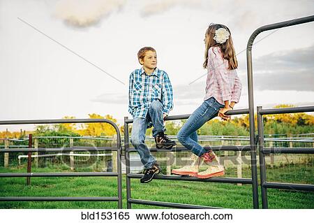 Stock Photography - Caucasian children sitting on fence on farm. Fotosearch