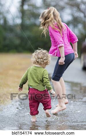 Picture - Caucasian children splashing in puddle. Fotosearch