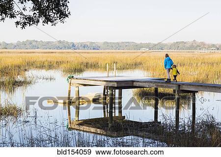 Stock Photo - Caucasian children walking on wooden dock over lake. Fotosearch
