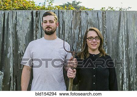 Picture - Caucasian couple holding pitchfork near fence. Fotosearch
