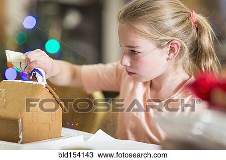 Stock Image - Caucasian girl decorating gingerbread house. Fotosearch