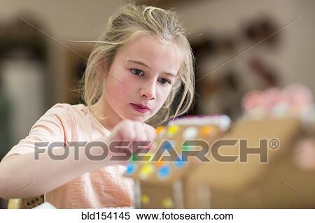 Stock Photography - Caucasian girl decorating gingerbread house. Fotosearch