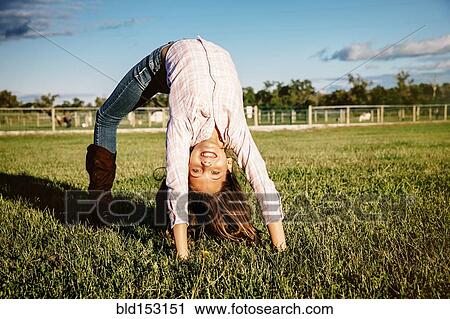 Stock Image - Caucasian girl doing bridge in field on ranch. Fotosearch