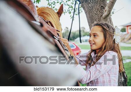 Caucasian girl fastening saddle on horse View Large Photo Image Stock Photo - Caucasian girl fastening saddle on horse. Fotosearch