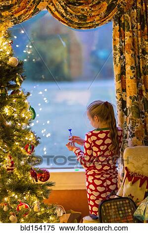 Stock Photography - Caucasian girl opening present near Christmas tree. Fotosearch