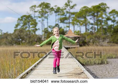 Stock Image - Caucasian girl running on wooden walkway. Fotosearch