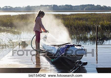 Stock Image - Caucasian girl spraying canoe on wooden dock over lake. Fotosearch