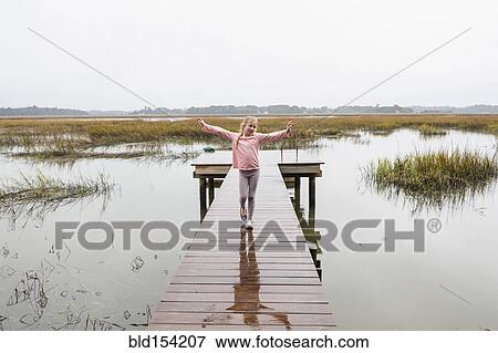 Stock Photo - Caucasian girl standing on wooden dock over lake. Fotosearch