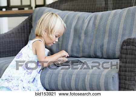 Stock Image - Caucasian girl using digital tablet on sofa. Fotosearch
